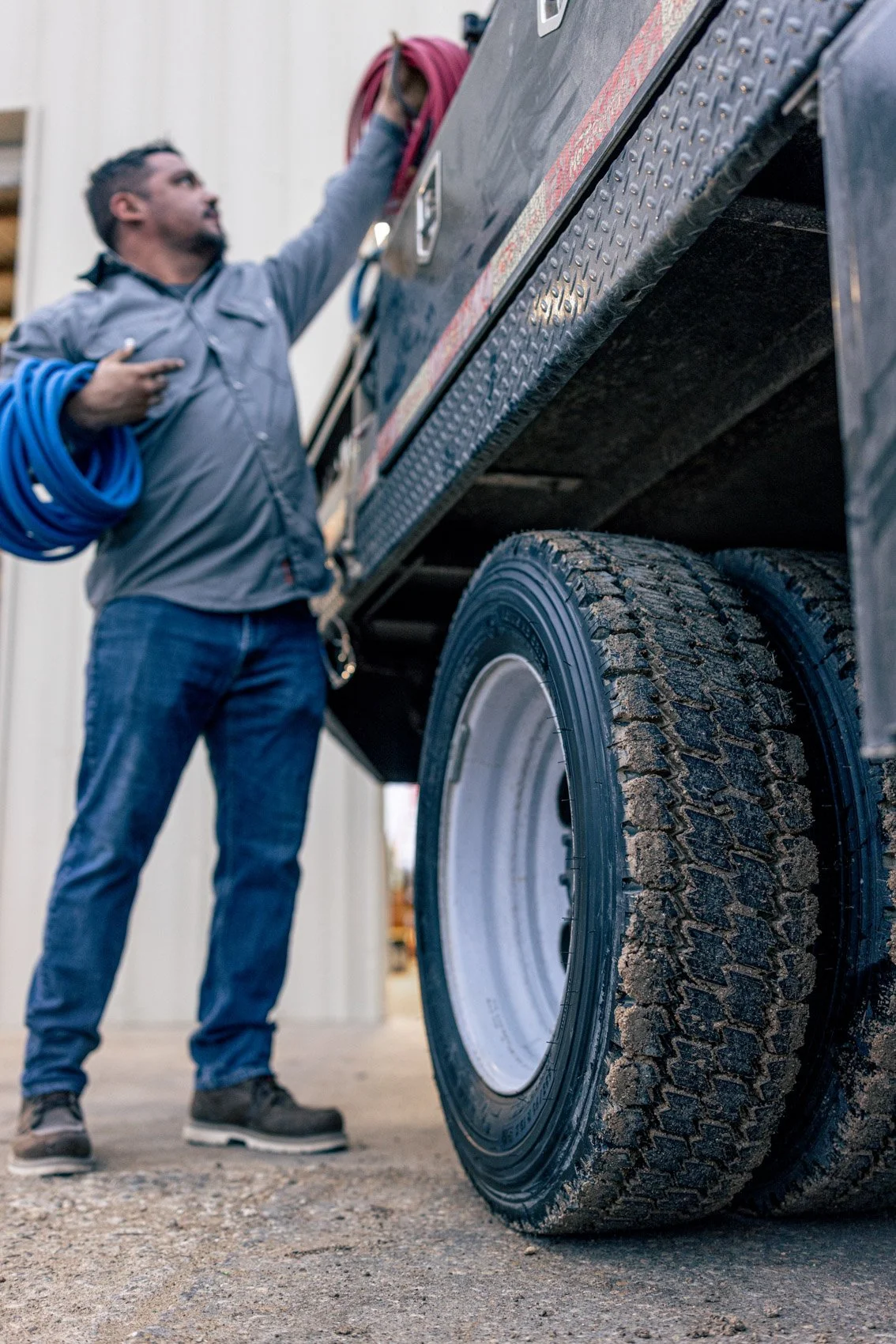 A man in work clothes is checking the front tire of a large truck in a workshop or garage.