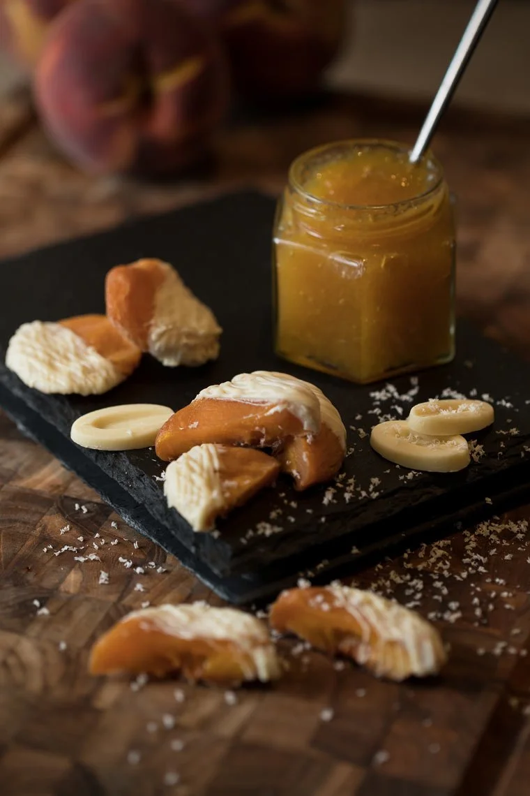 Assorted cheeses, a jar of cheese spread, and crackers on a black slate board with a wooden table background.