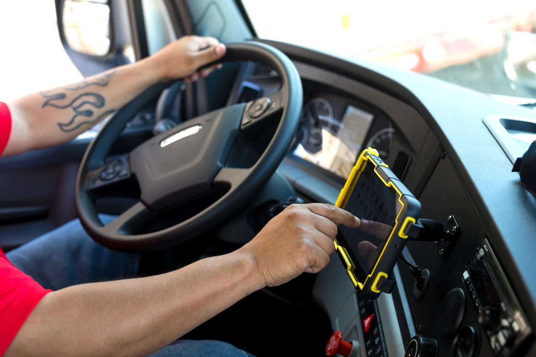 A person driving a truck while using a rugged tablet mounted on the dashboard.