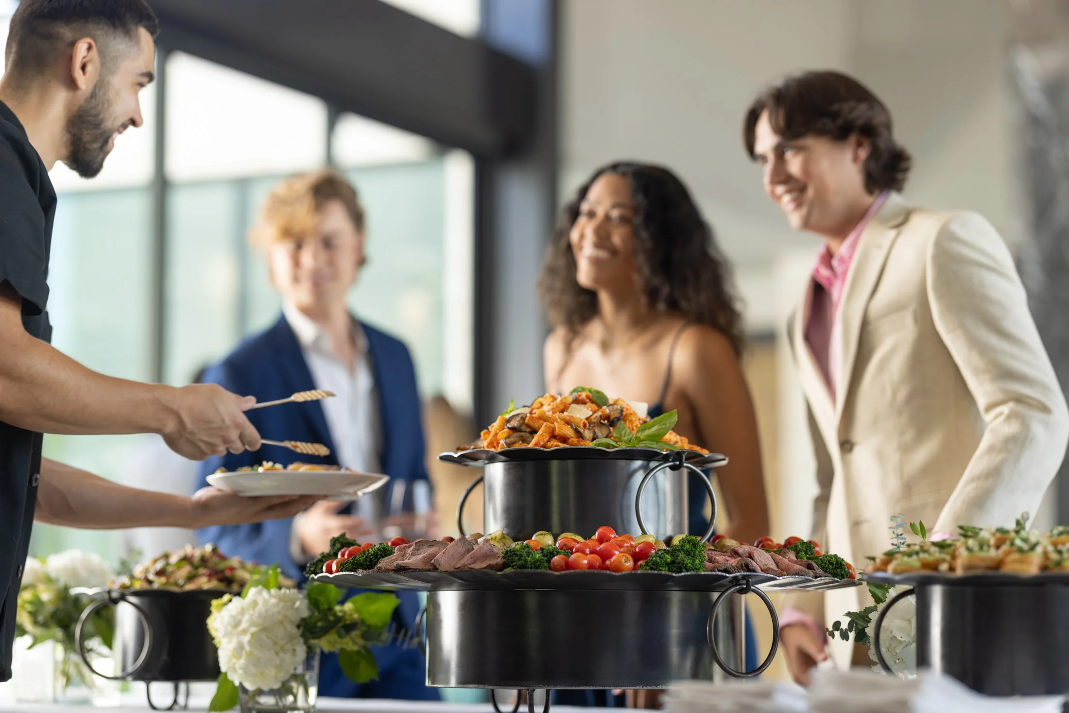 People at a buffet table selecting food, with various dishes including salads and grilled items, in a bright and modern indoor setting.