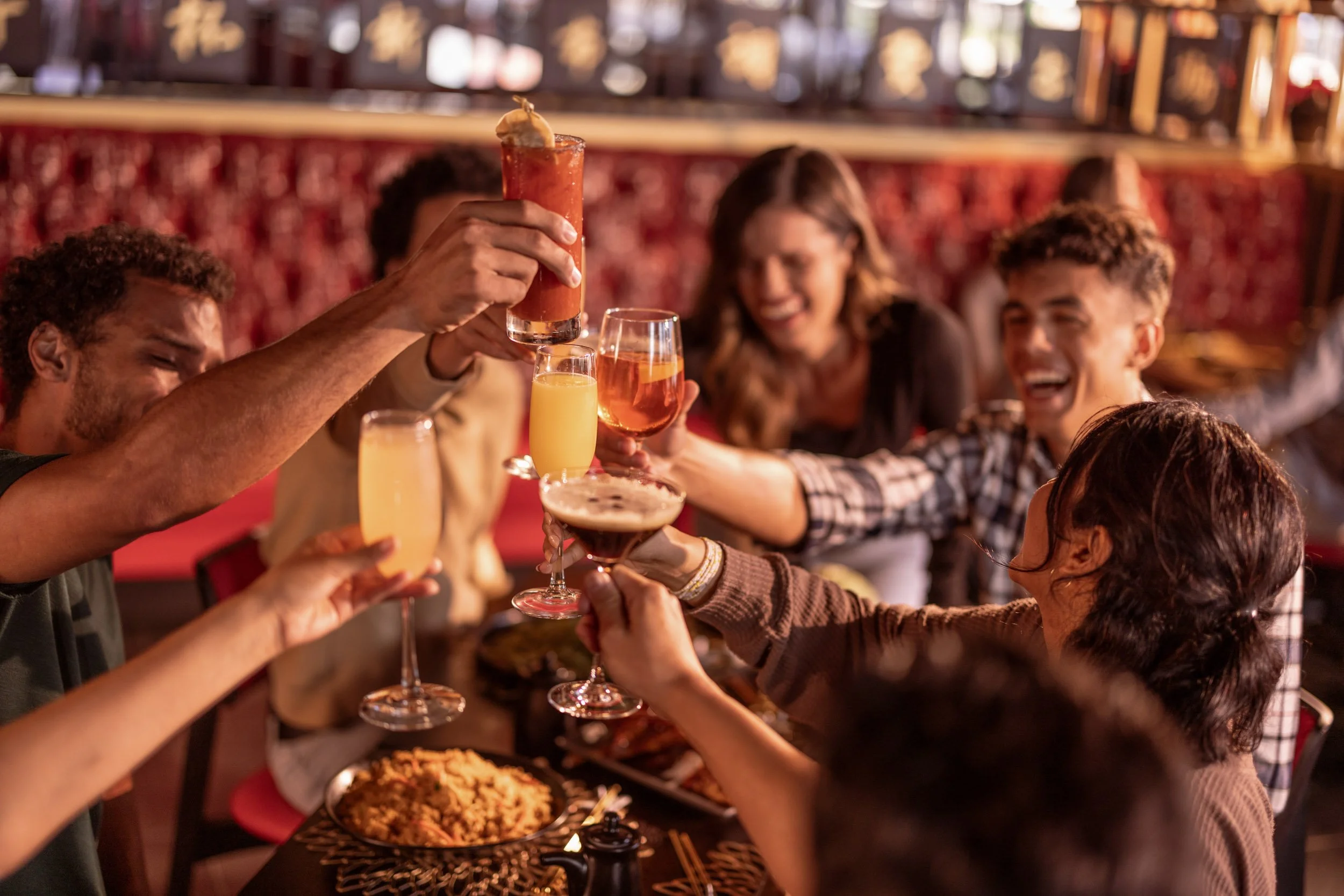 A group of people celebrating, raising drinks in a toast at a restaurant or bar.