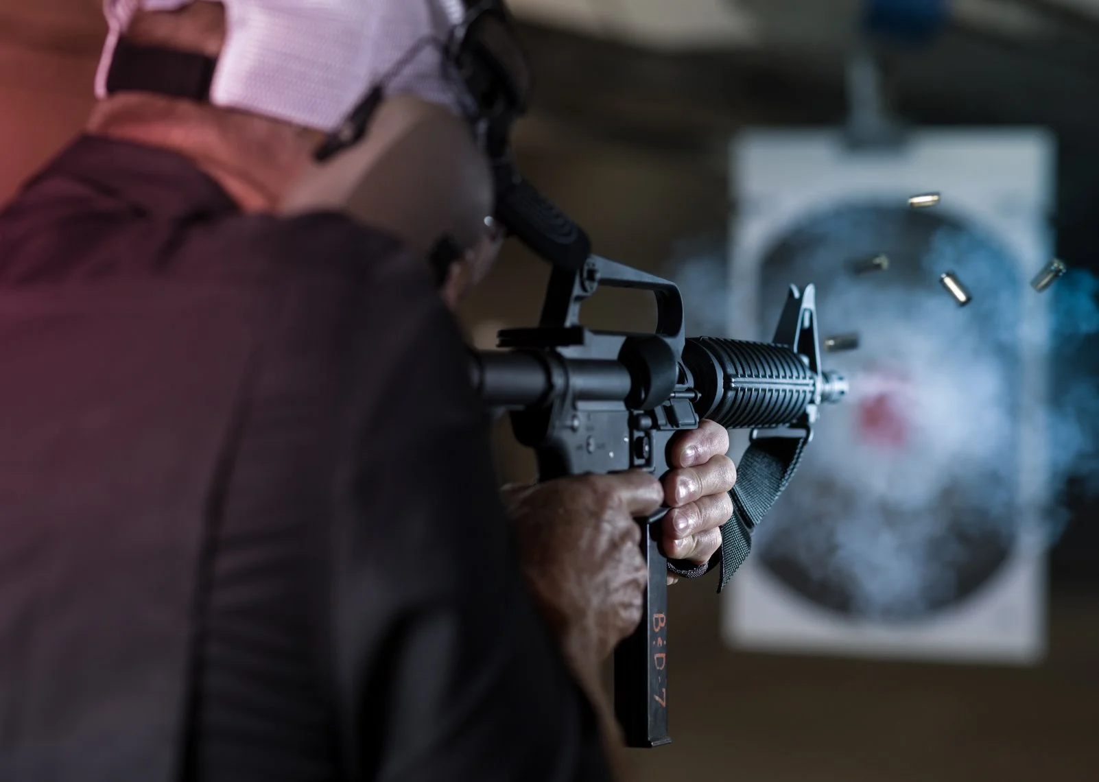 Person firing a semi-automatic rifle, bullets being ejected, at an indoor shooting range.