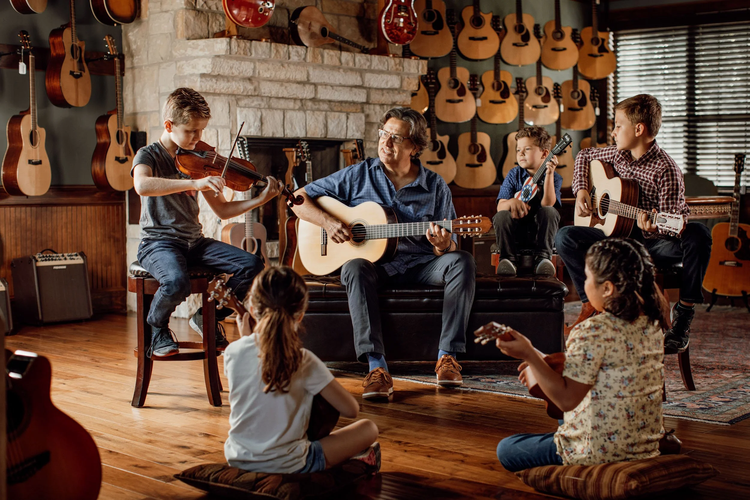 A group of children and a man playing musical instruments in a room with many guitars on the wall.