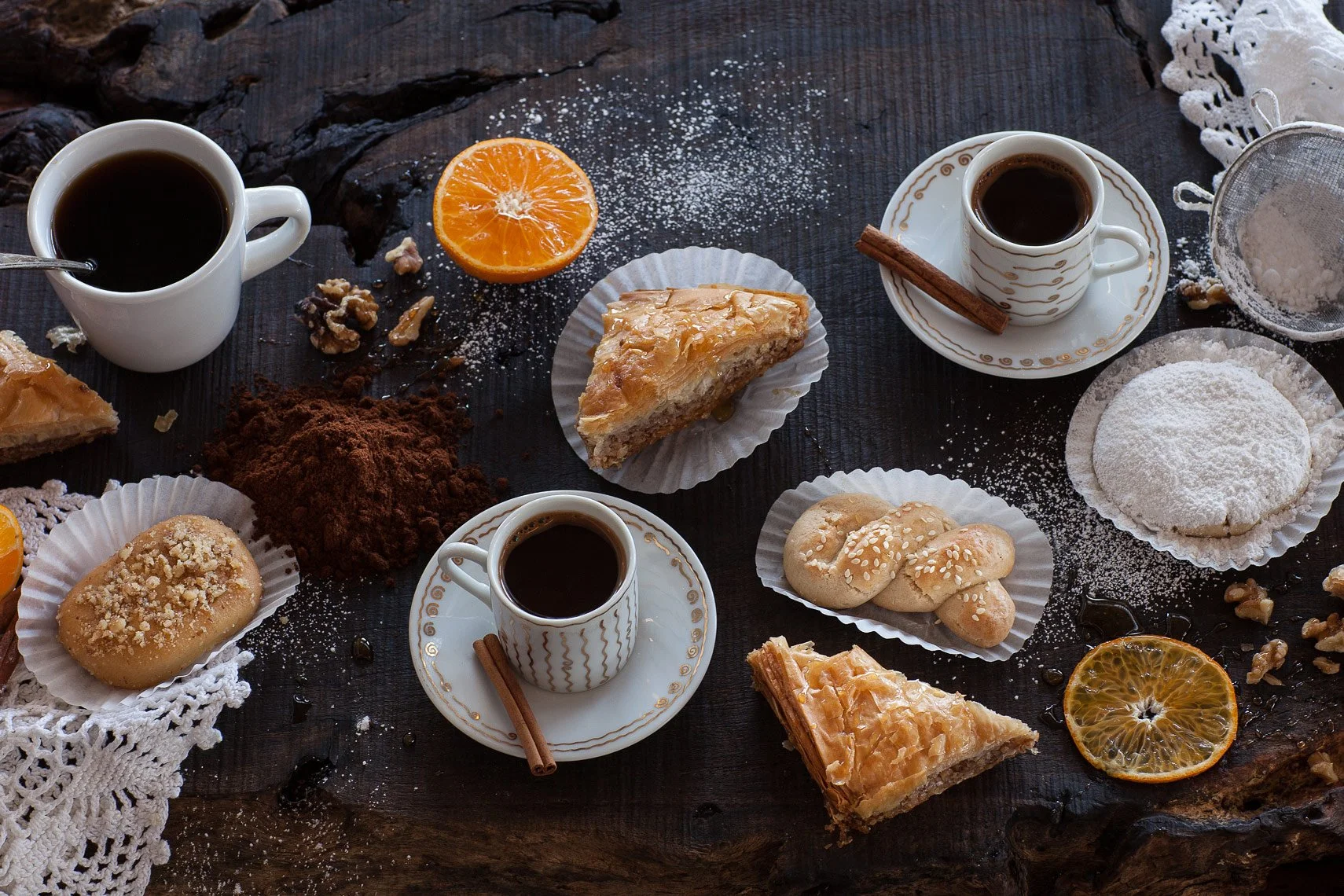 Assorted desserts and coffee on a dark wooden table, including slices of pie, cookies, oranges, and cups of black coffee.