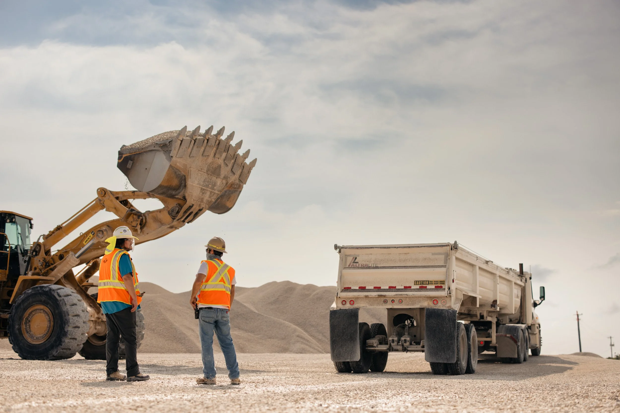 Construction workers wearing safety vests and helmets standing near a large construction vehicle during daytime.
