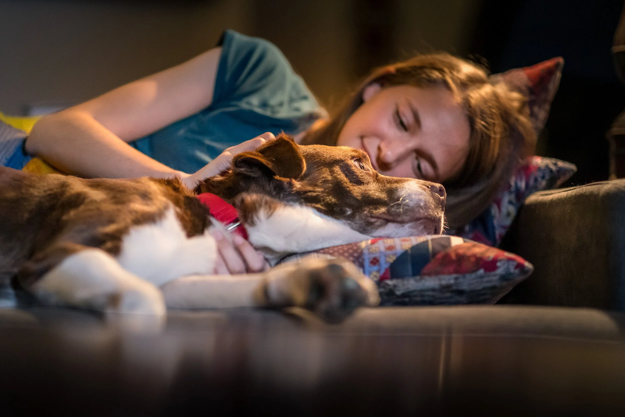 A woman lying on a bed cuddling with her dog.