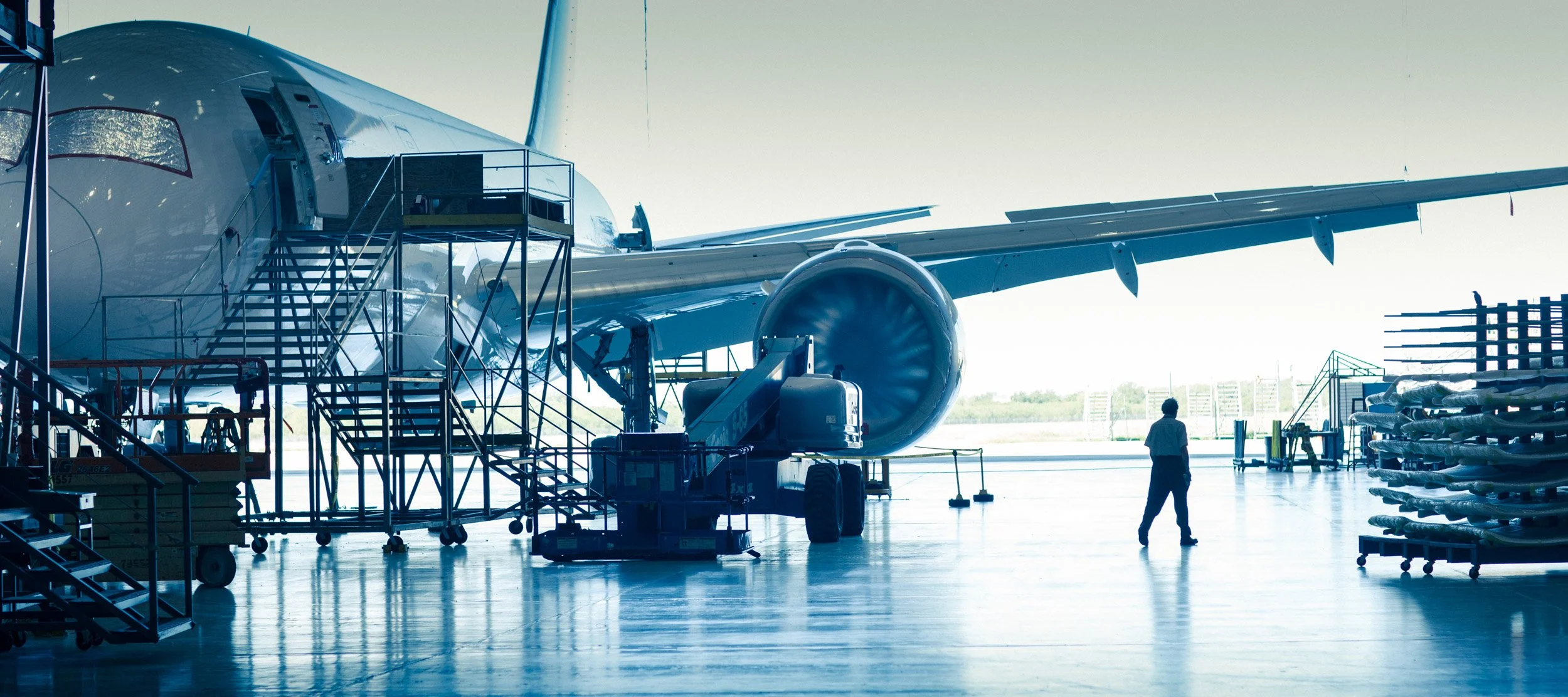 An airplane inside a hangar with maintenance equipment and a person walking nearby.