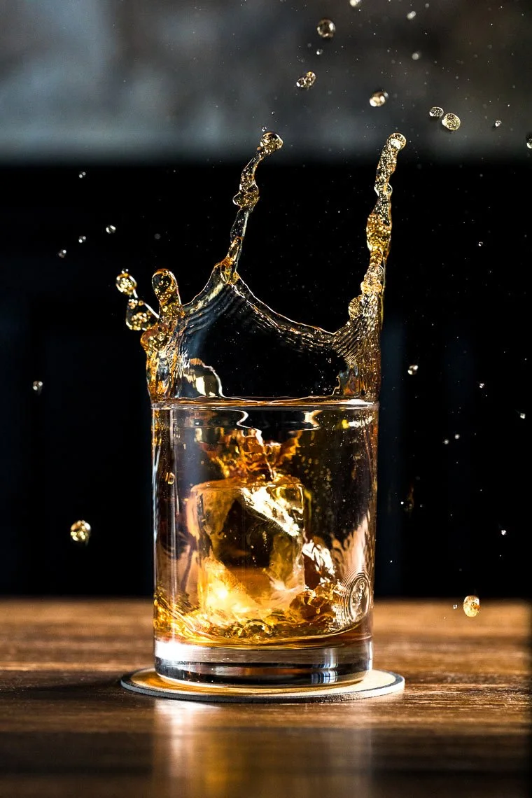 A glass of whiskey with ice cubes, splashing as a splash rises above the rim.