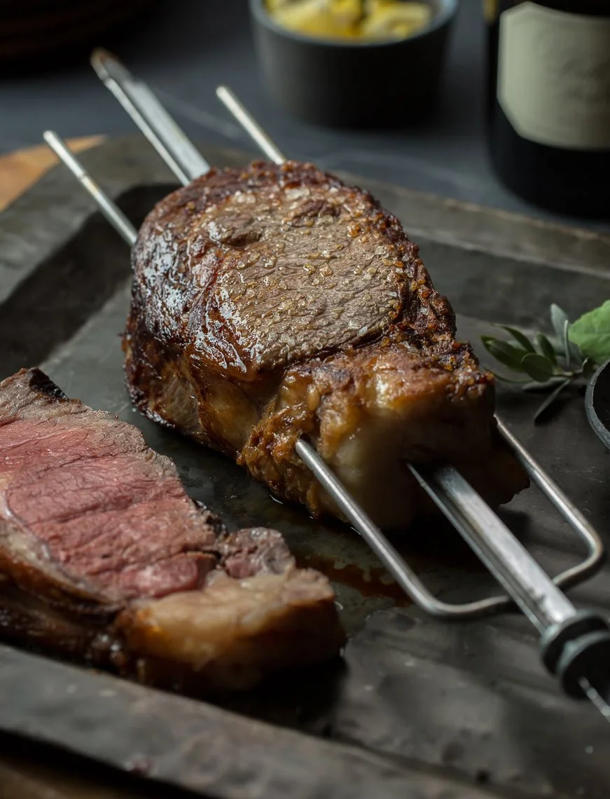 A rack of cooked prime rib roast with one slice cut and placed on a tray.