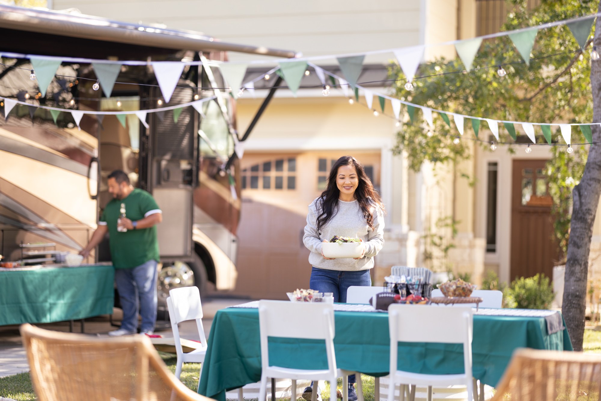 A woman holding a salad tray at an outdoor gathering with decorations and tables, and a man in a green shirt nearby.