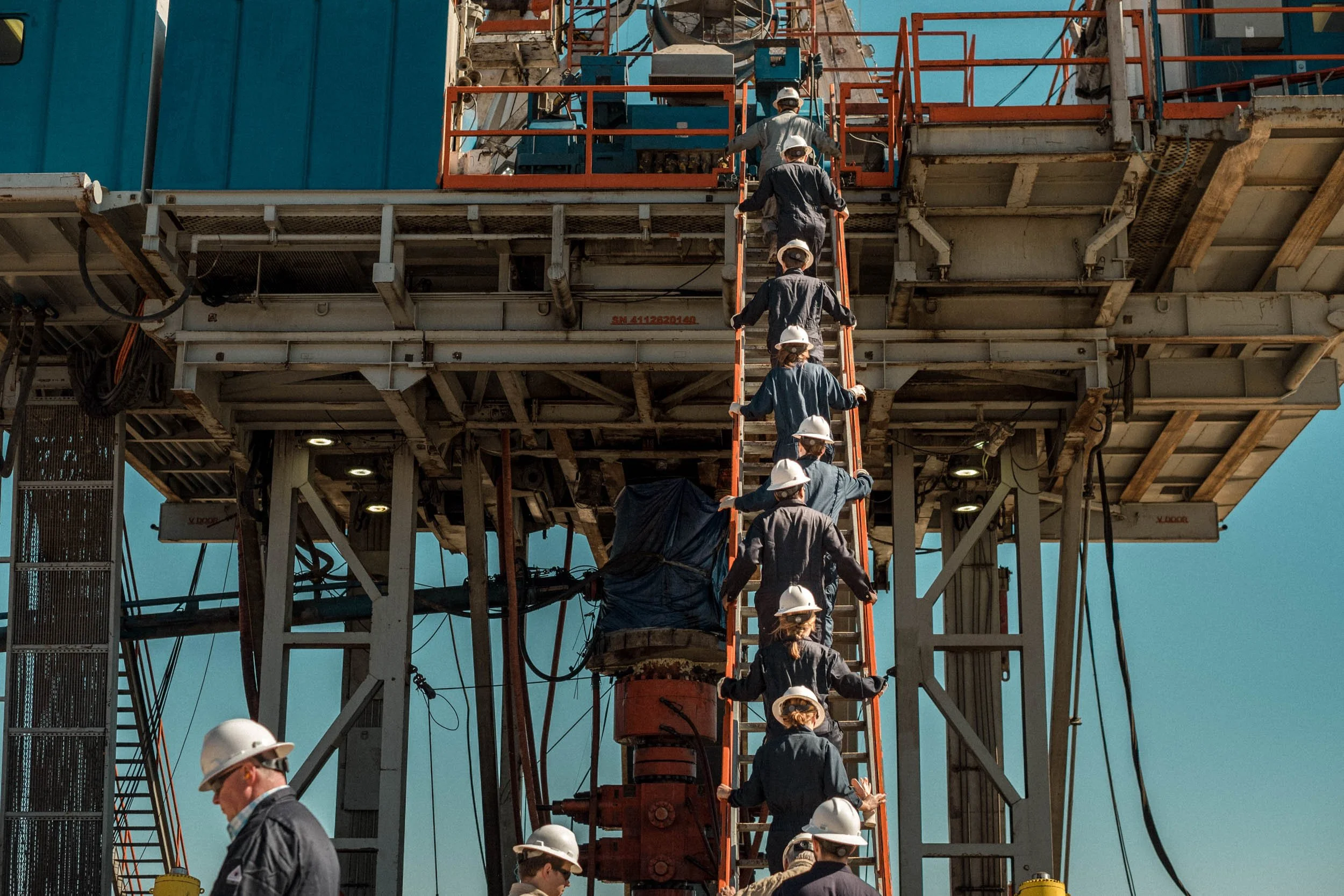 Construction workers wearing hard hats working on a building structure, climbing a ladder under a bright blue sky.