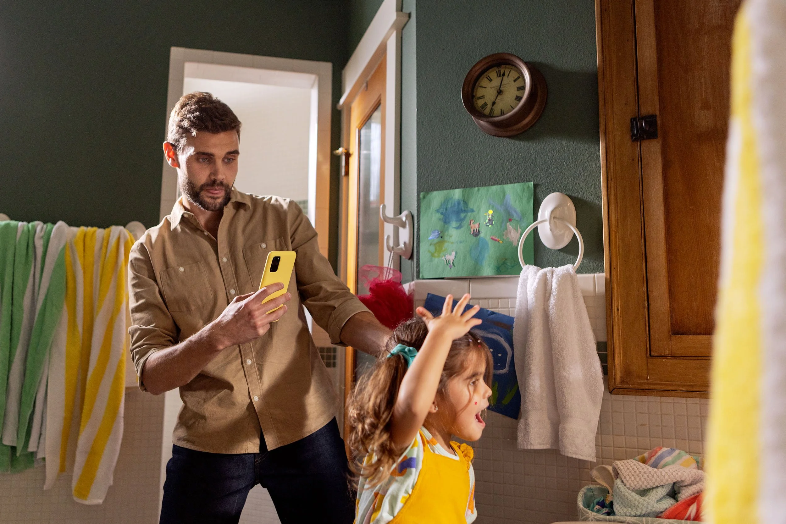 A man and two young girls in a laundry room, with the man looking at his phone and the girls pointing at something outside the frame.