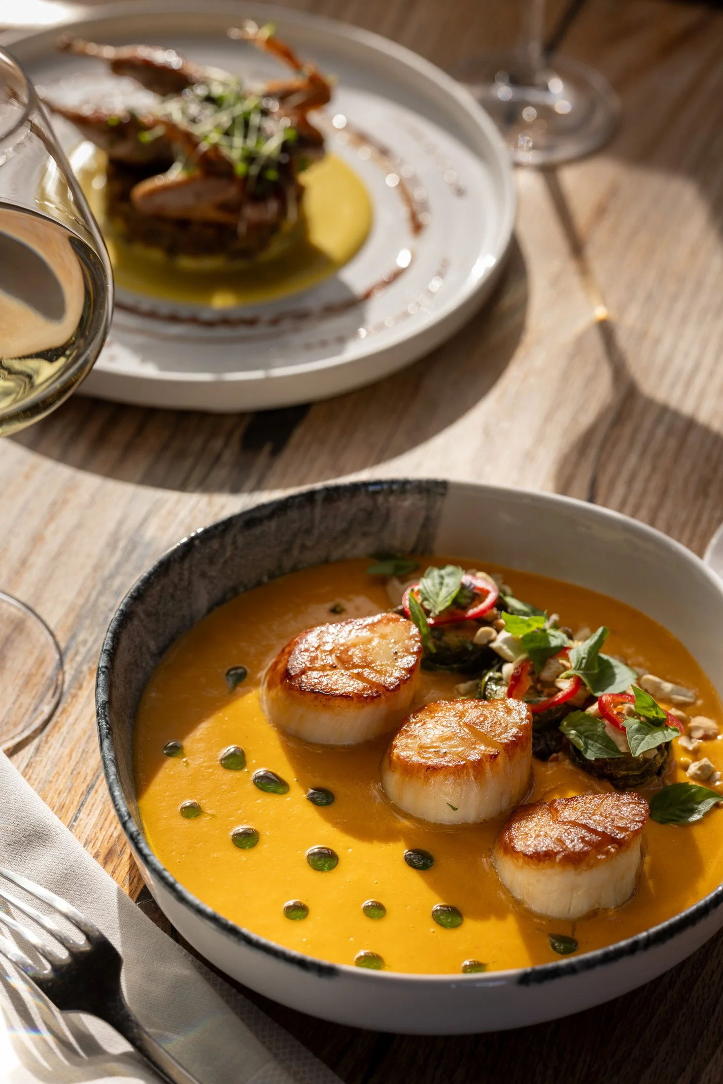 A bowl of creamy yellow soup topped with seared scallops and garnished with herbs and red chili slices.
