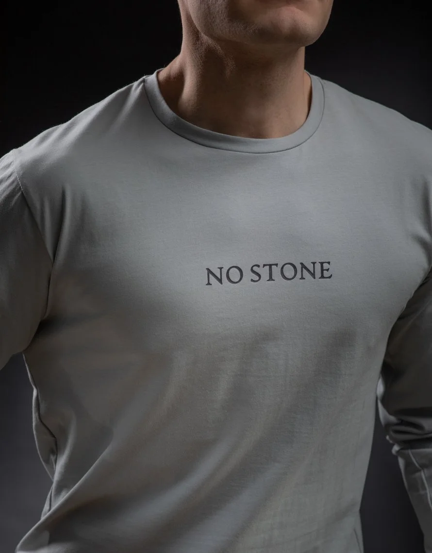 Close-up of a person wearing a gray T-shirt with the words "NO STONE" printed on the front.