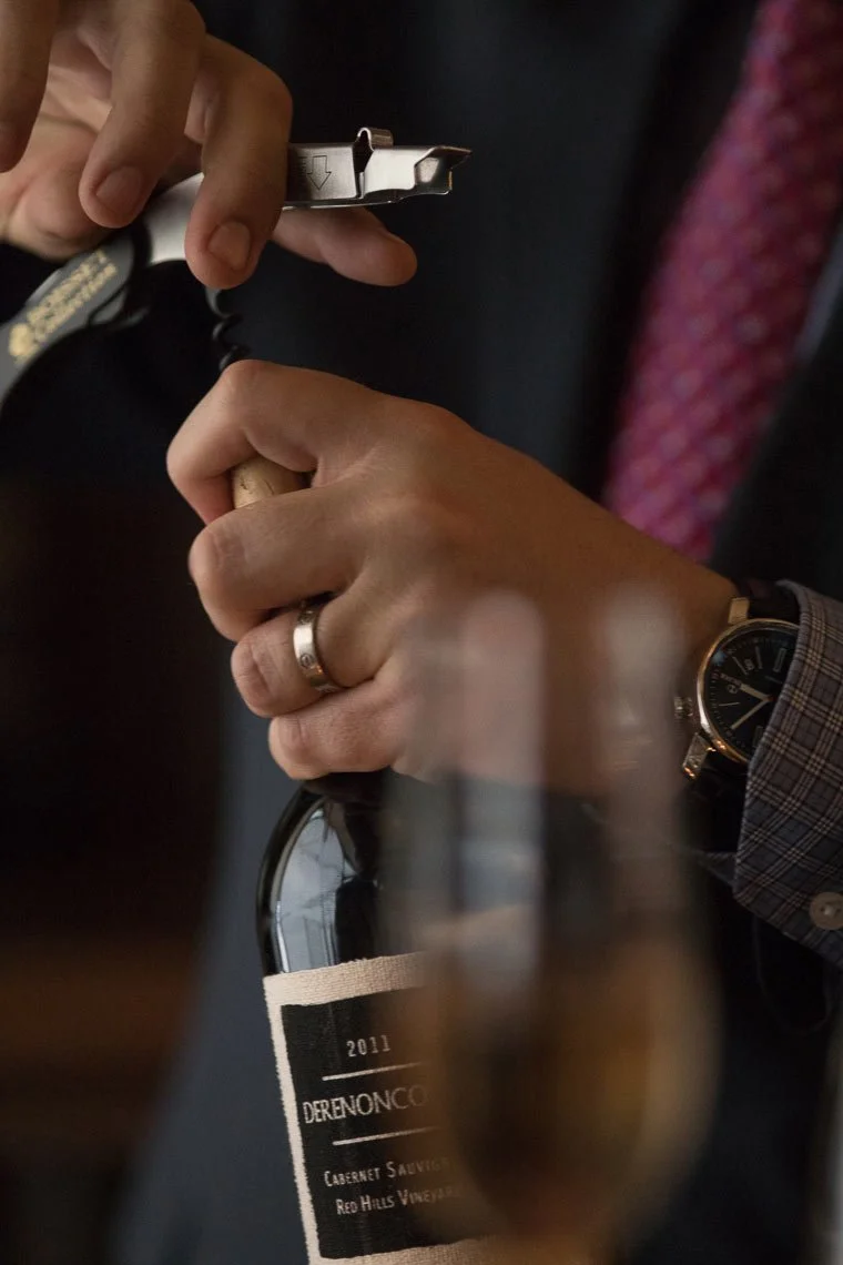 A person opening a bottle of Derenoncourt cabernet sauvignon wine.