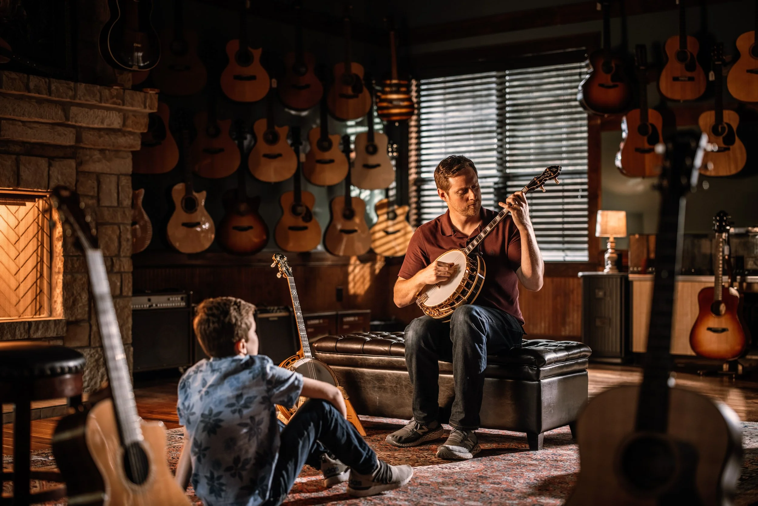 A music instructor playing a banjo and teaching two children in a guitar shop filled with hanging guitars and musical equipment.