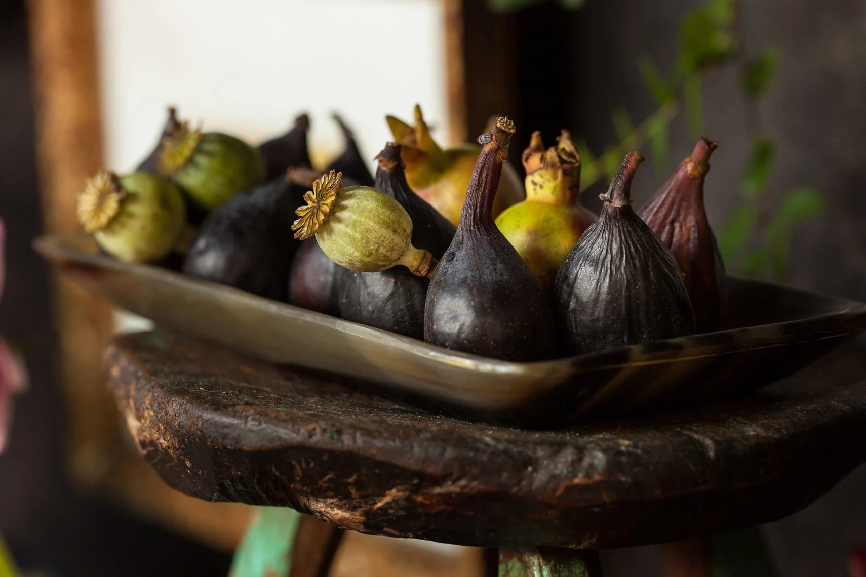 A metal tray with various types of figs, some green and some dark purple, placed on a rustic wooden surface.