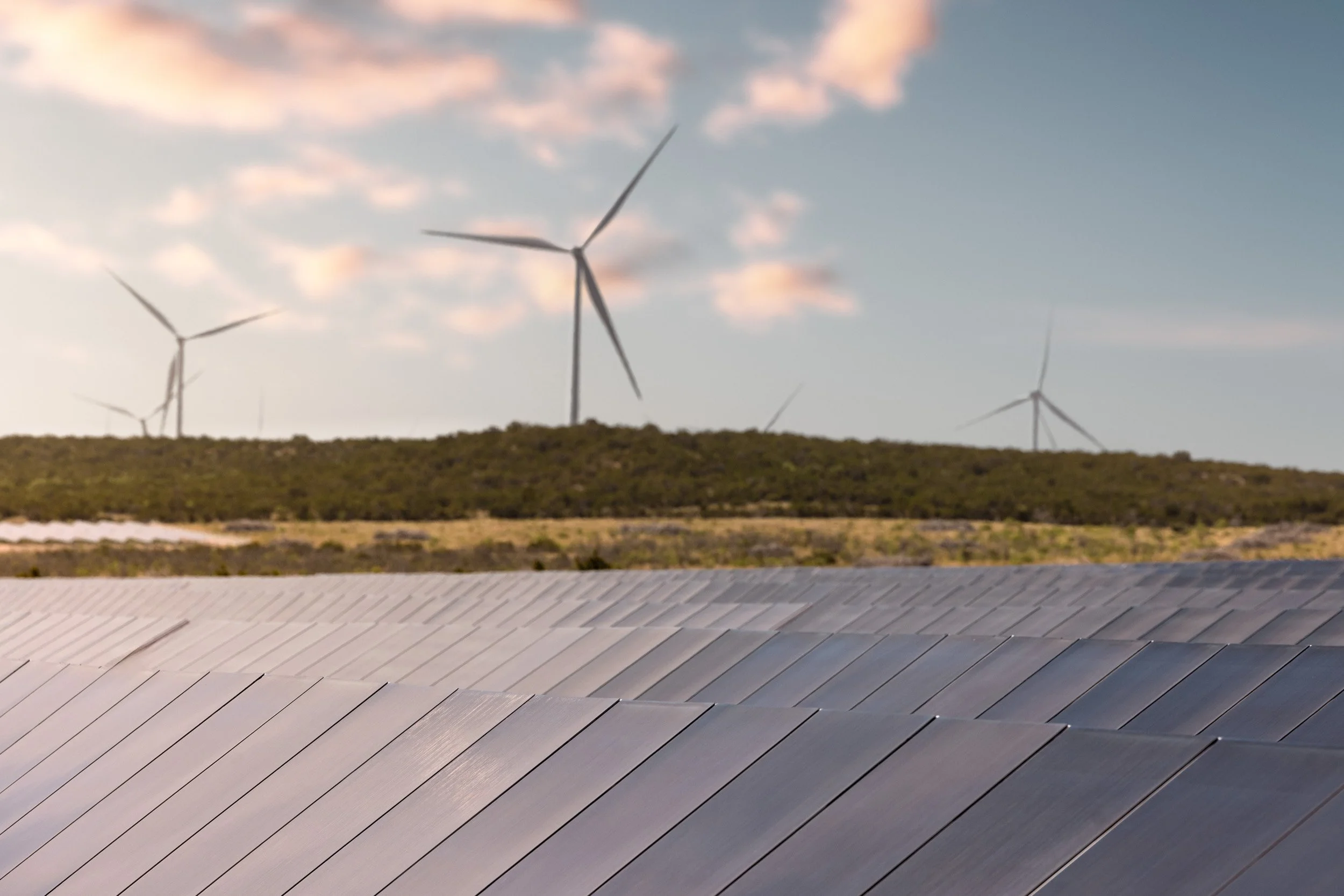 A landscape view showing wind turbines on a hillside under a sky with pink and orange clouds.
