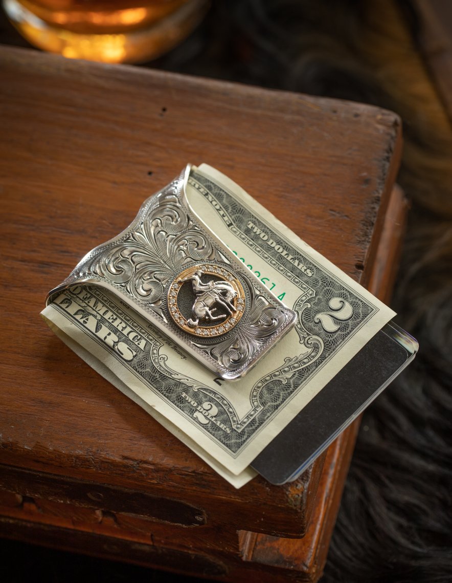 A stack of two-dollar bills, a keychain with a decorated silver and gold sheriff badge, and a black card on top of the bills, placed on a wooden surface.