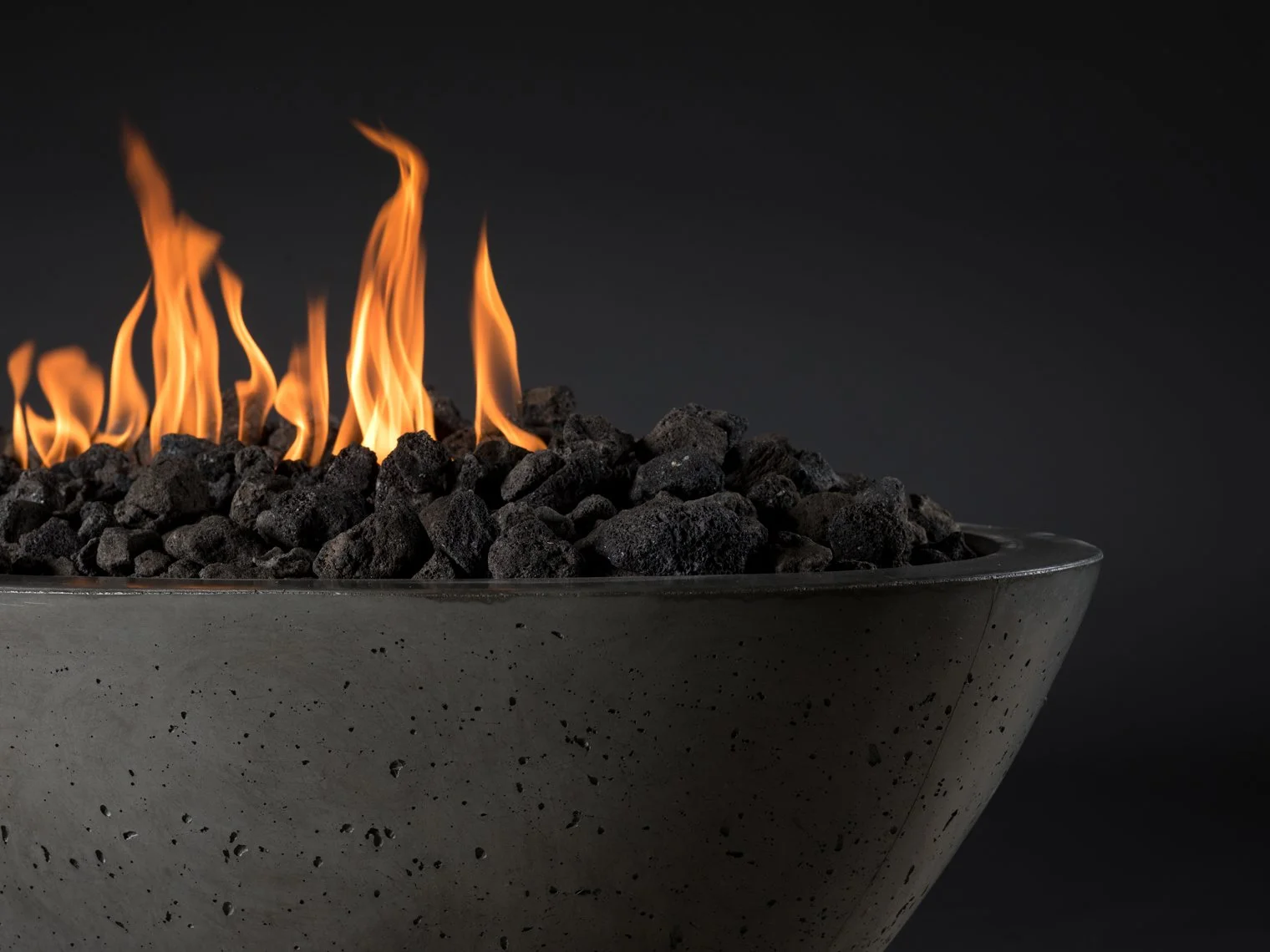 A modern fire pit with flames coming out of black rocks on a dark background.