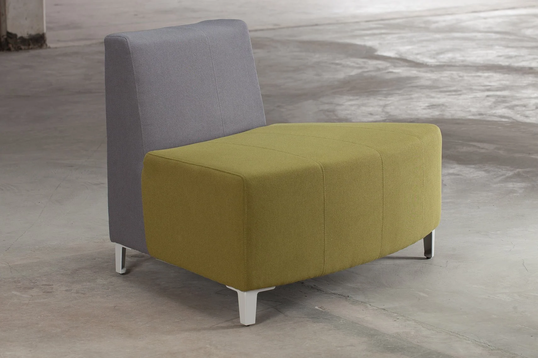 A modern, two-tone upholstered armchair with a gray backrest and a yellow seat, standing on four white metal legs in a minimalist, industrial-style space with wooden flooring.