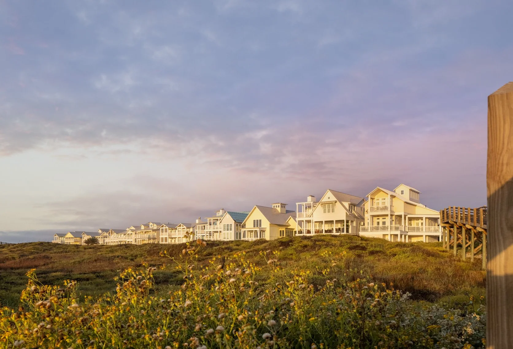 Row of beach houses on a hill under a partly cloudy sky at sunset.