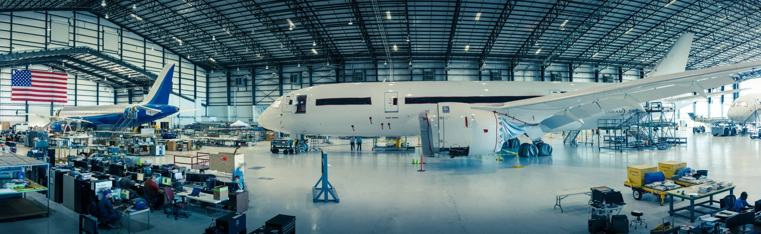 Large airplane inside a spacious aircraft hangar under construction or maintenance, with various equipment, tools, and workers around.