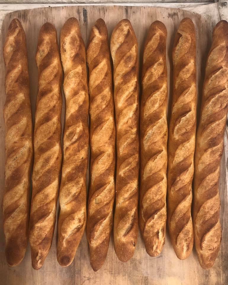 Nine freshly baked French baguettes with twisted tops lined up on a wooden surface.