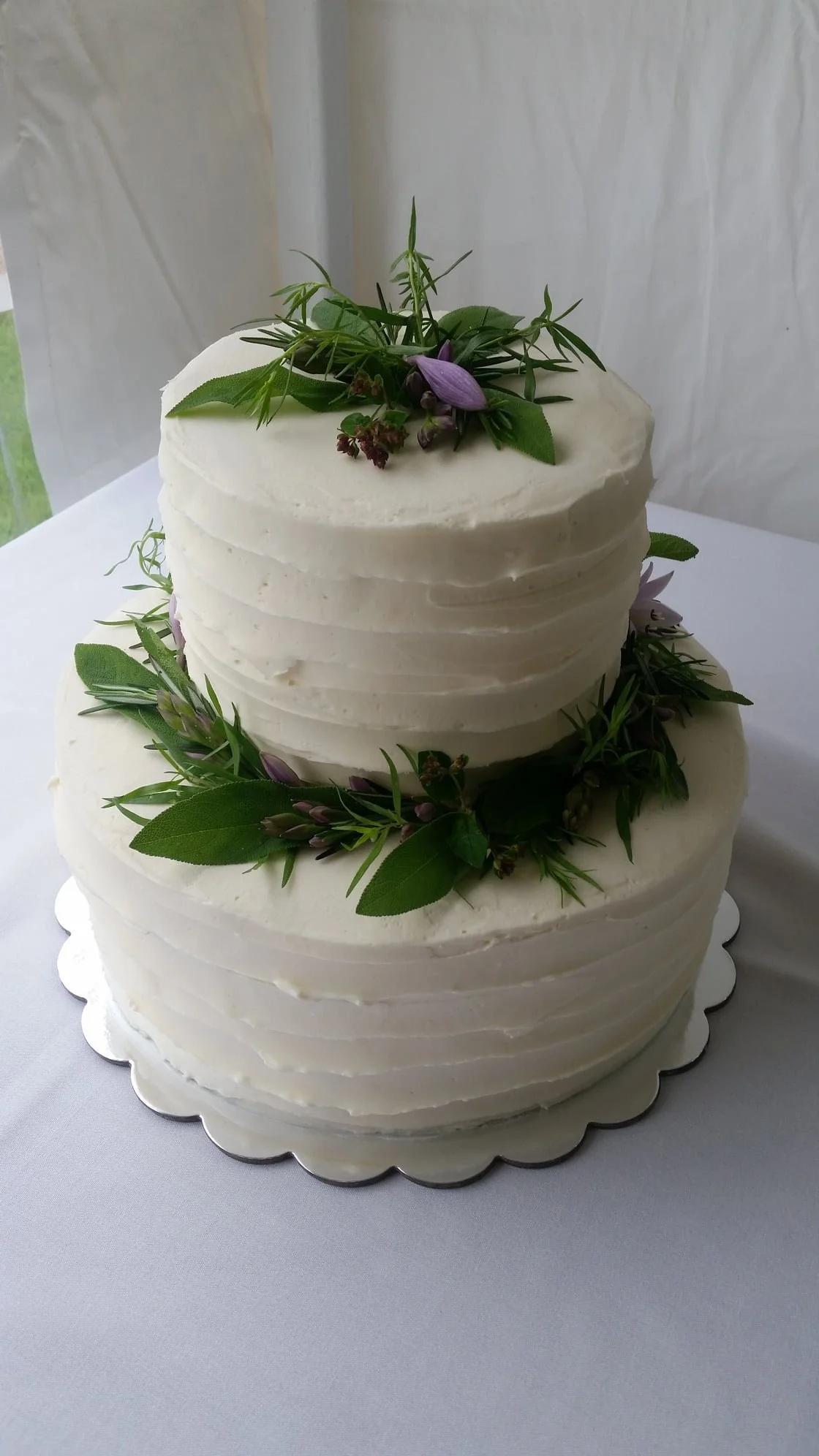 Two-tiered white wedding cake decorated with green leaves and purple flowers.