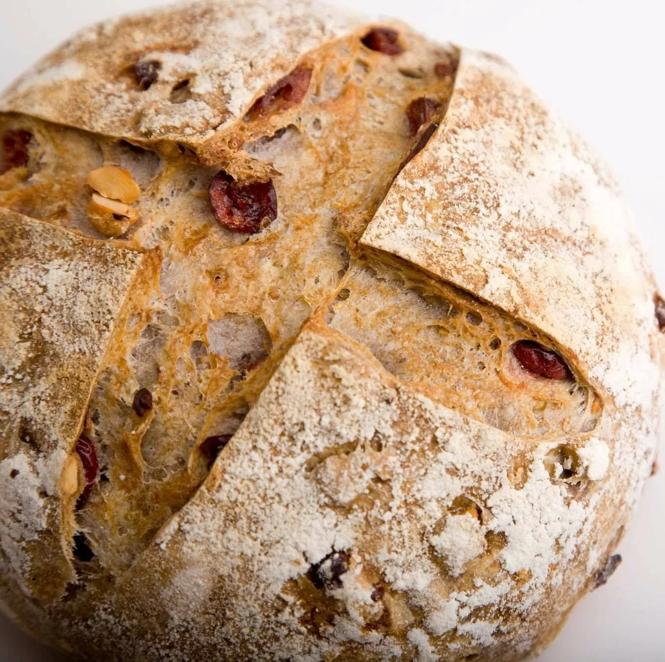 A close-up of a round loaf of bread with a dusting of flour on top, cut to show a soft interior with raisins and nuts.