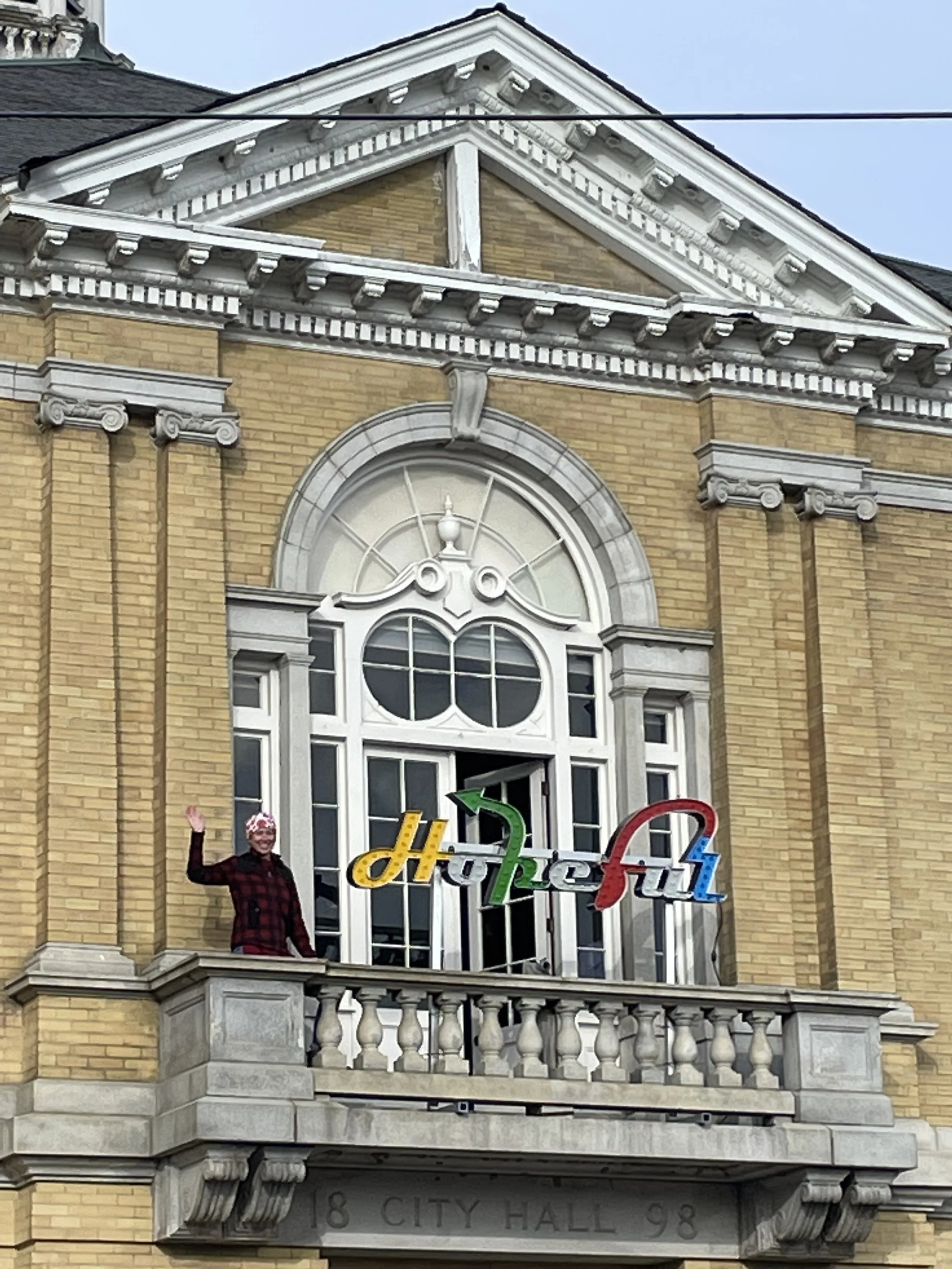 Image of Maureen AuCoin on the balcony of Hallowell City Hall next to the "Hopeful" sign by Charlie Hewitt.