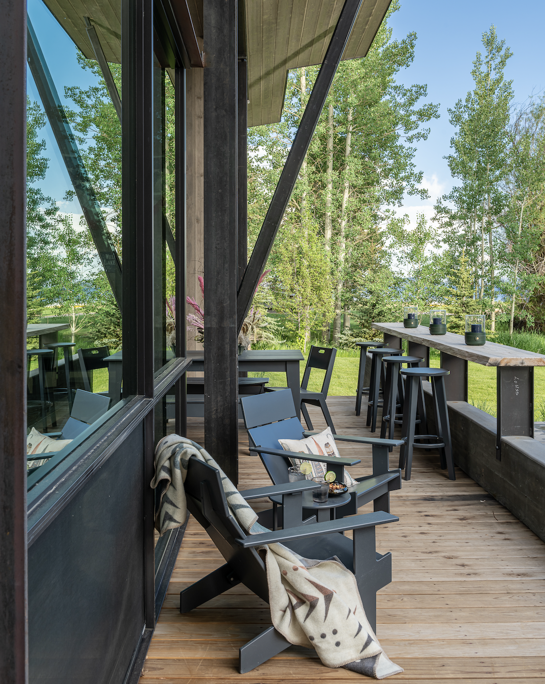 Covered deck with adironack chairs and bar seating and steel supports overlooking Hebgen Lake