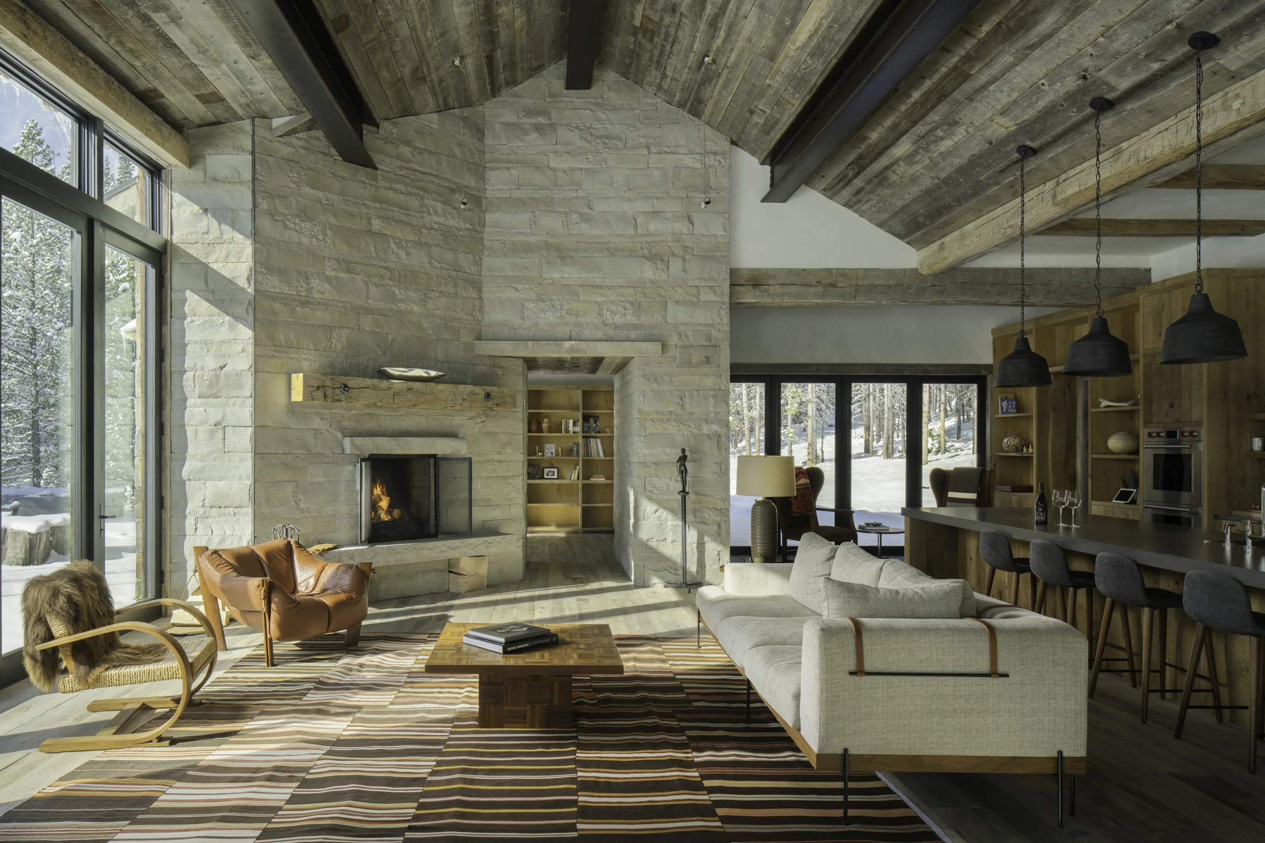 Living room with floor to ceiling stone fireplace wood ceiling and open layout in Big Sky Montana