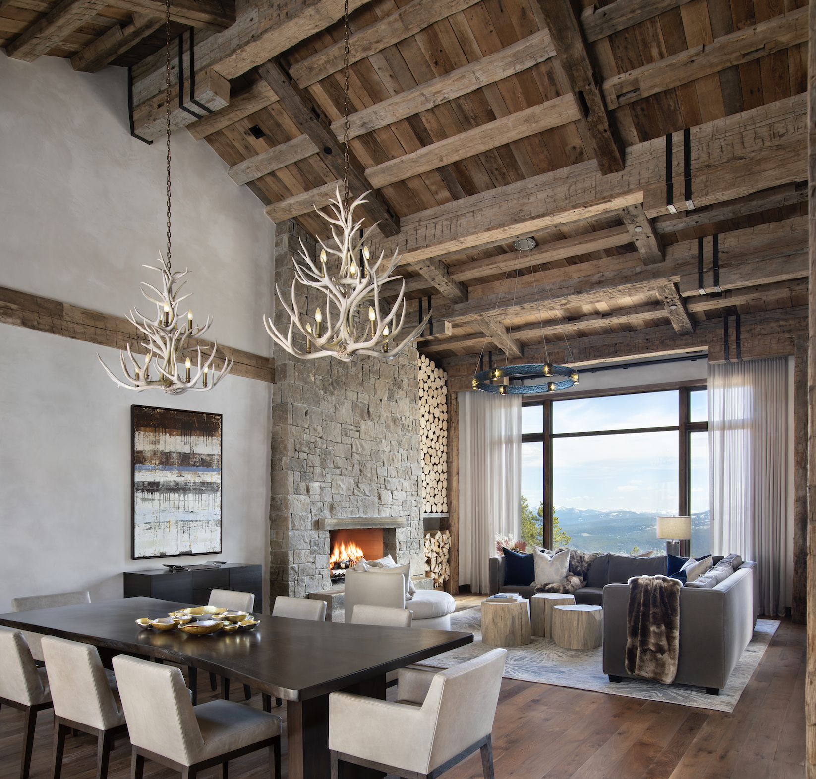 Open dining and living area with reclaimed timber structure, stone fireplace, and mountain views beyond.