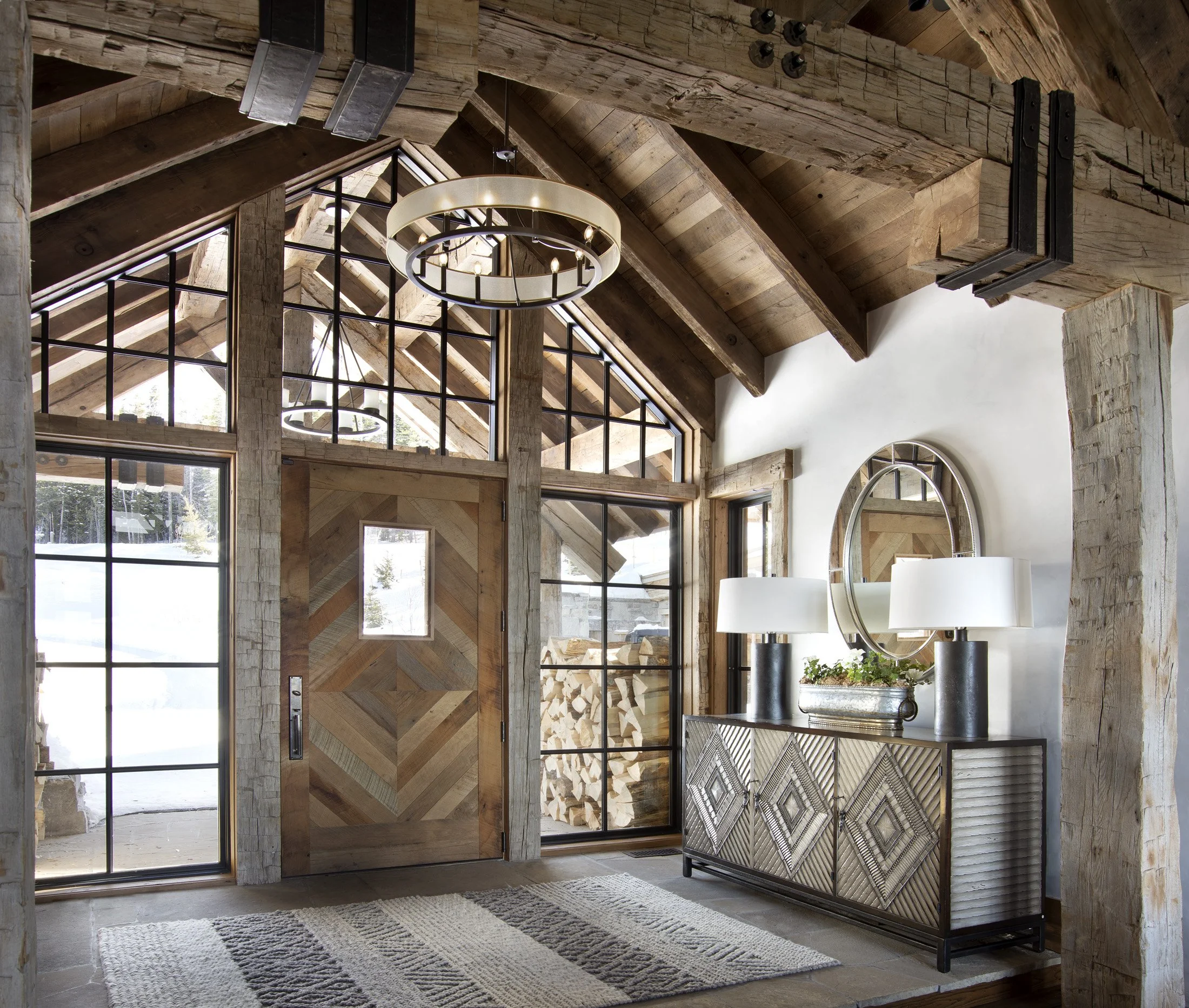 Interior entry with heavy timber beams, glass doors, and stone flooring at mountain home in Big Sky Montana