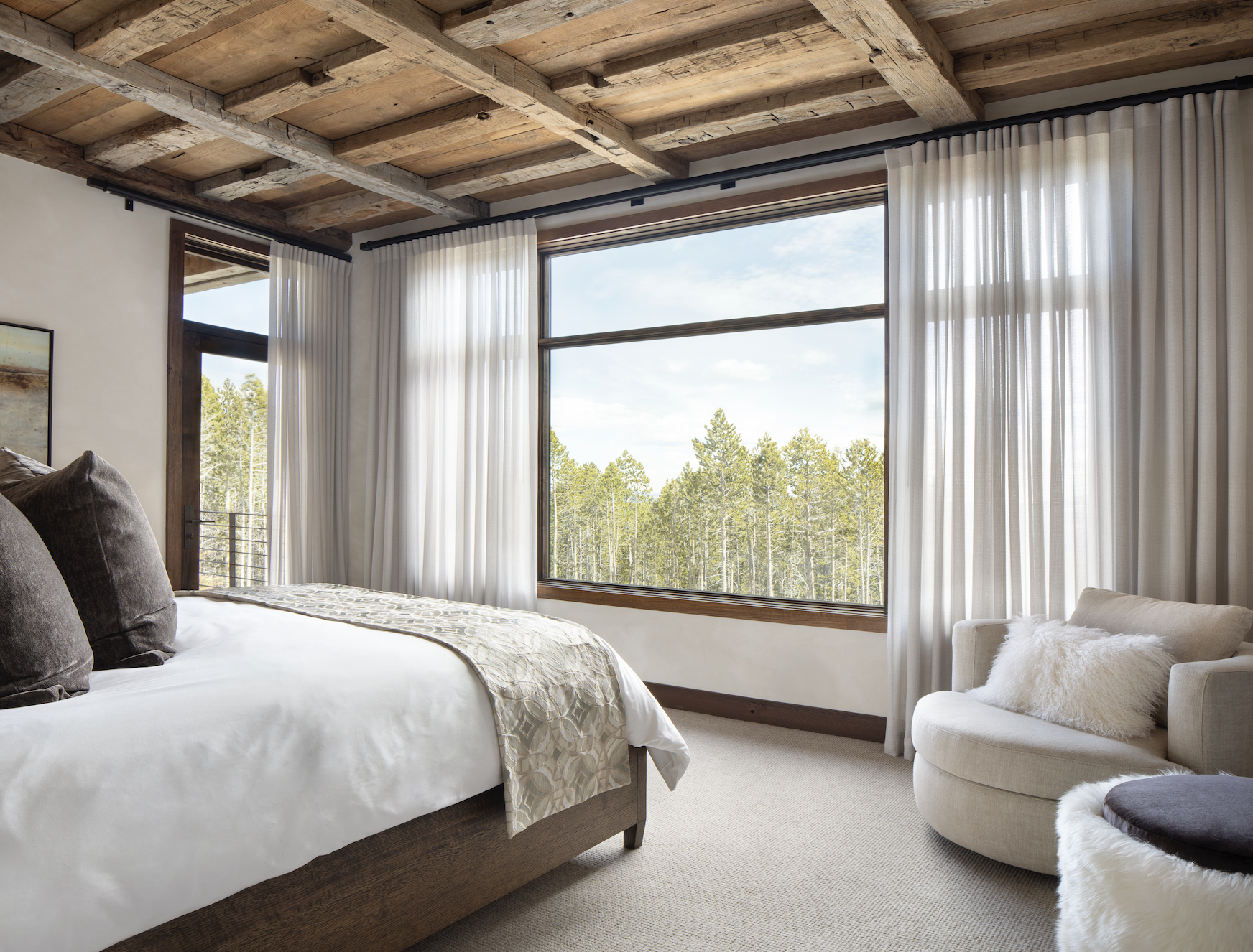Bedroom with reclaimed timber ceiling, large picture window, and views into the forest.
