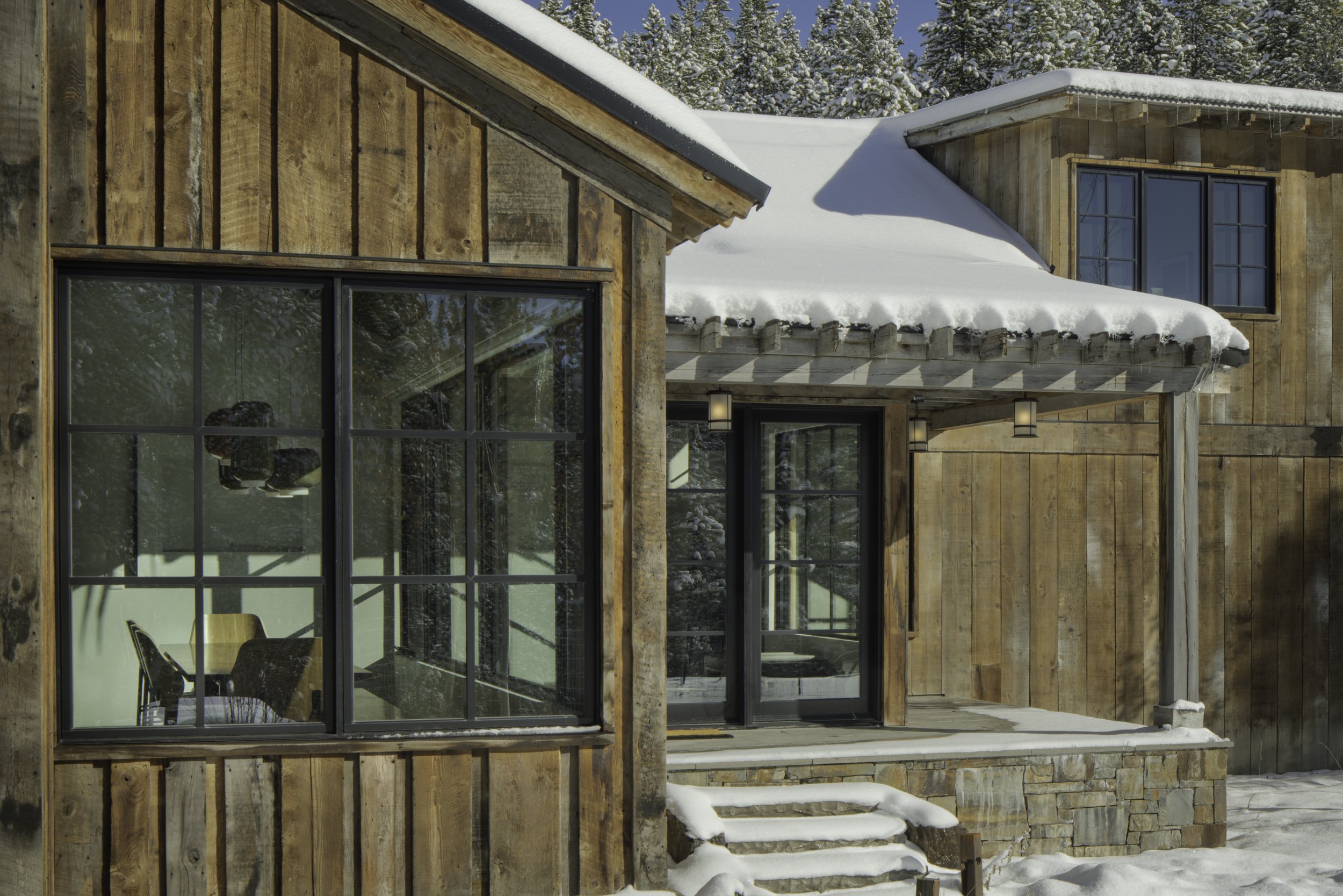  Snow-covered home exterior with wood siding and stonework in Spanish Peaks Big Sky Montana