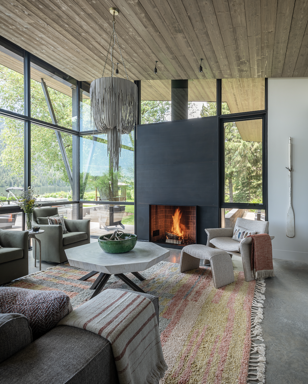Living room with modern fireplace, wood ceiling, and large windows overlooking the lake