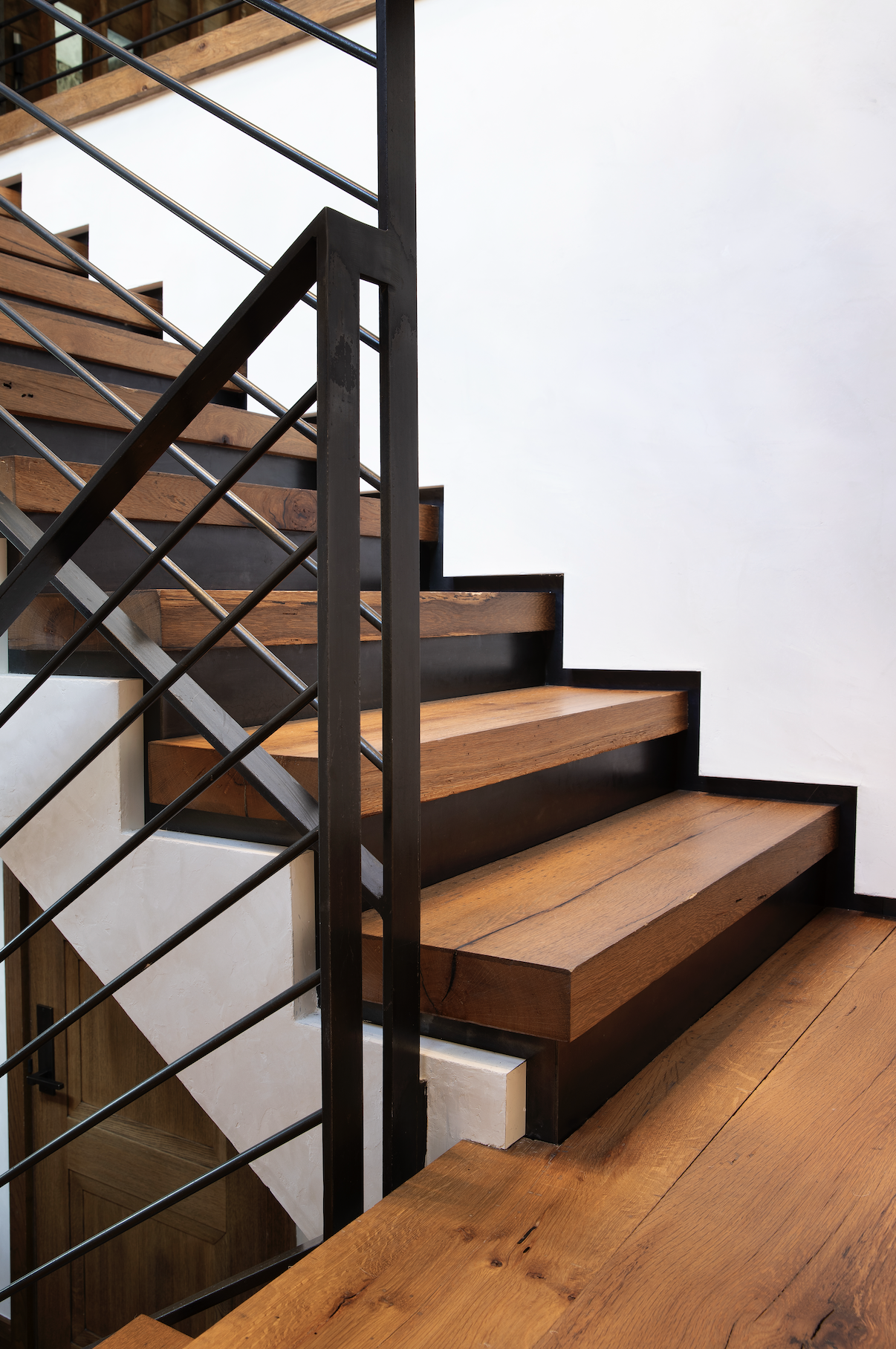Stair landing with steel railing, reclaimed timber wall cladding, and stone fireplace visible beyond in a custom mountain home.