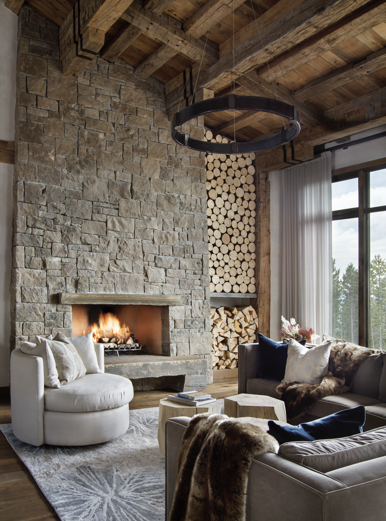 Living room with stone fireplace, reclaimed timber beams, and large windows overlooking mountain views.