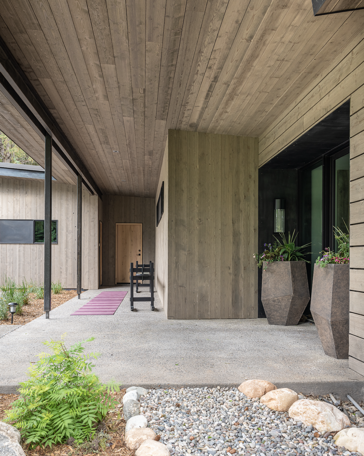 Covered entry walkway with wood siding, steel columns, and concrete path