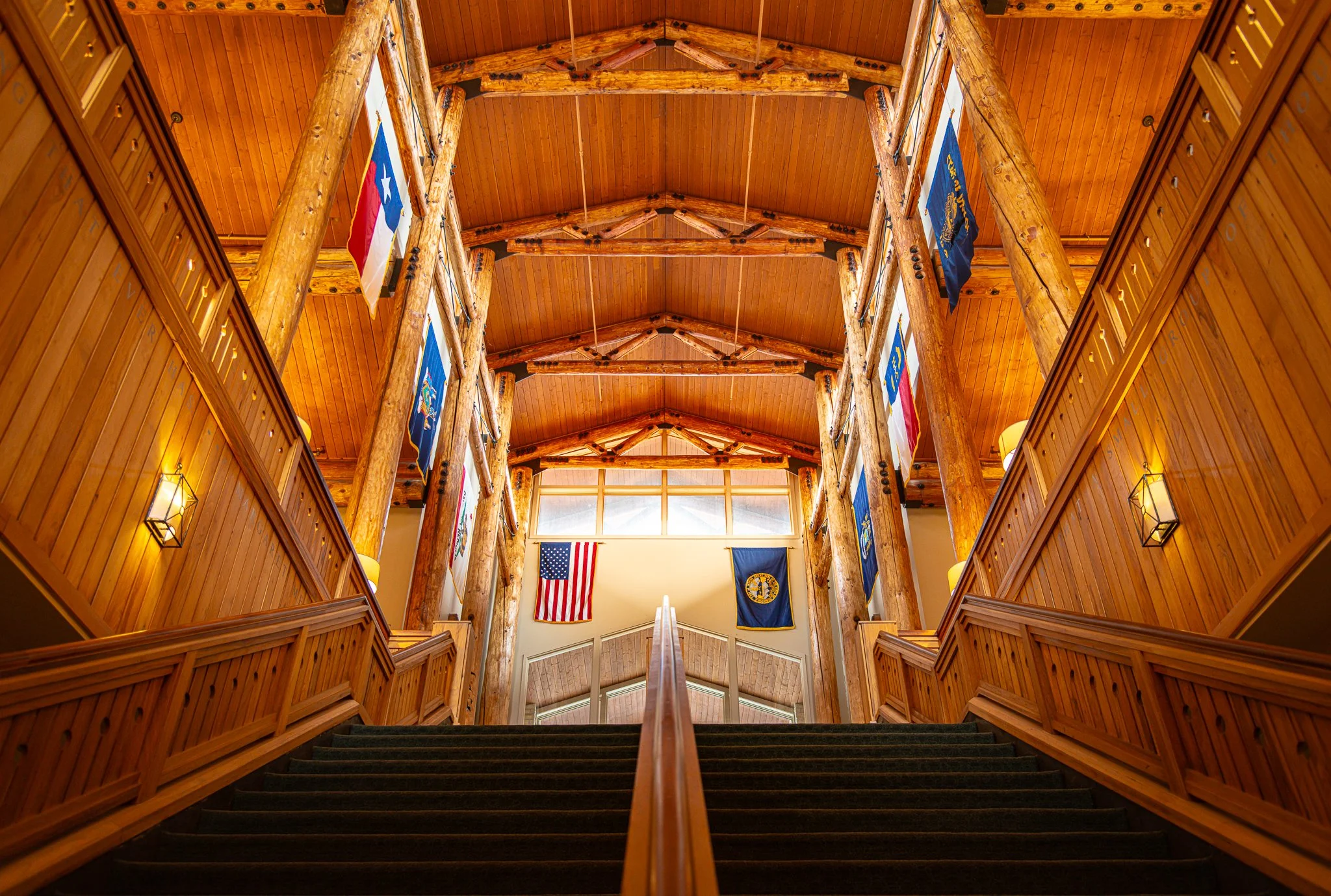 Staircase leading to a balcony or upper level inside a wooden building with flags hanging from the ceiling.