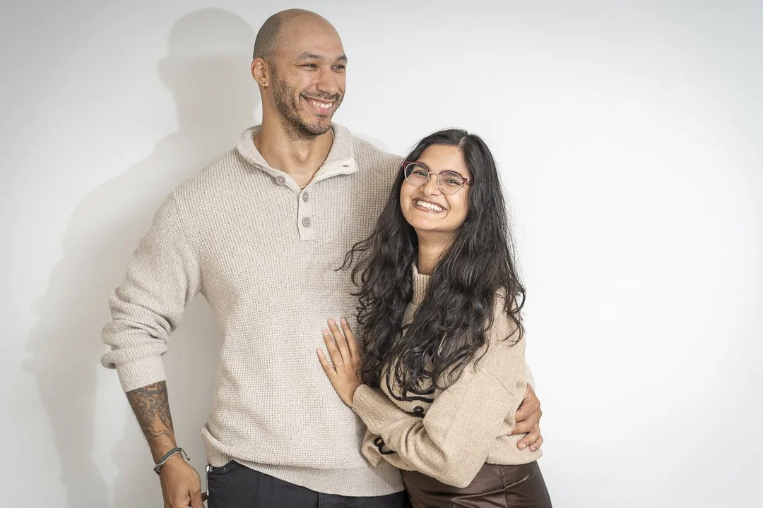 A man and woman smiling and embracing each other against a white background.