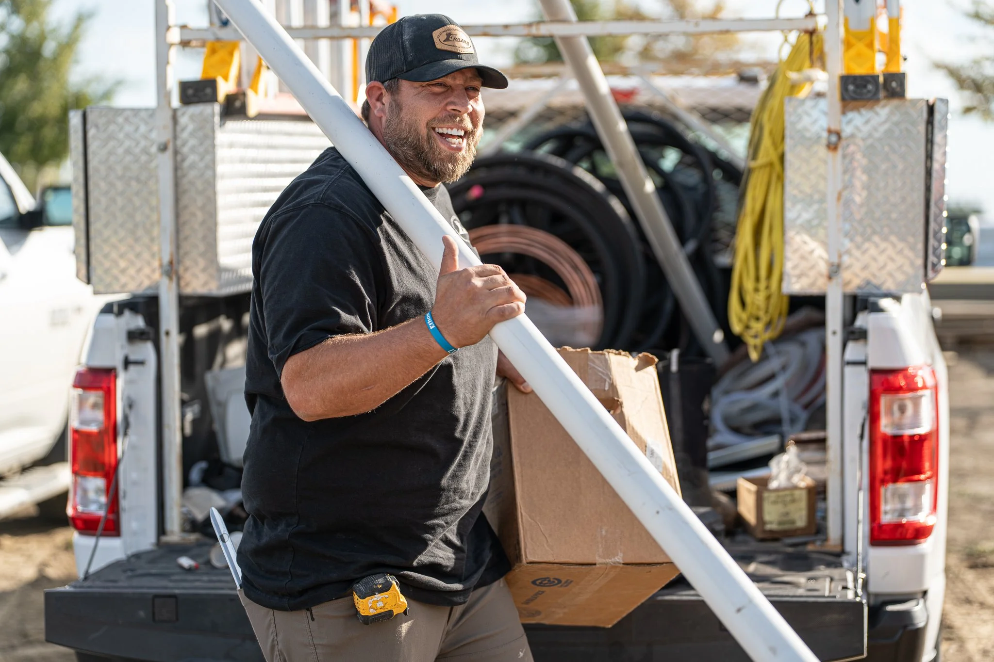 A man holding a pole and a cardboard box standing next to a pickup truck with equipment in the background.
