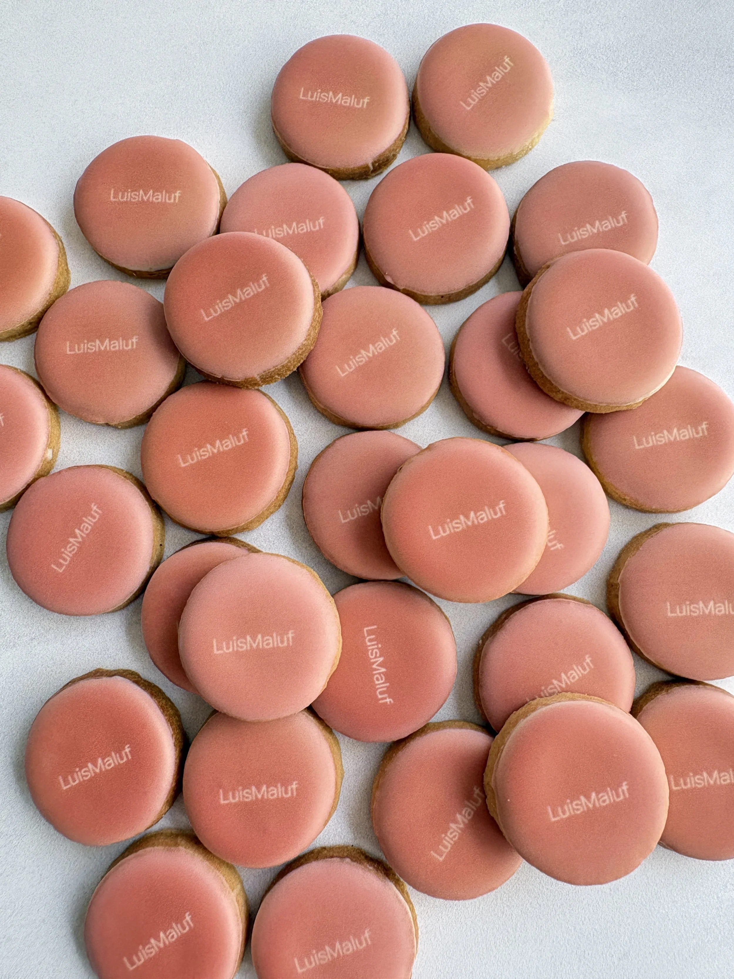 Conjunto de biscoitos personalizados com glacê a marca 'Galeria LuisMaluf' impressa em cima, dispostos sobre uma superfície branca.