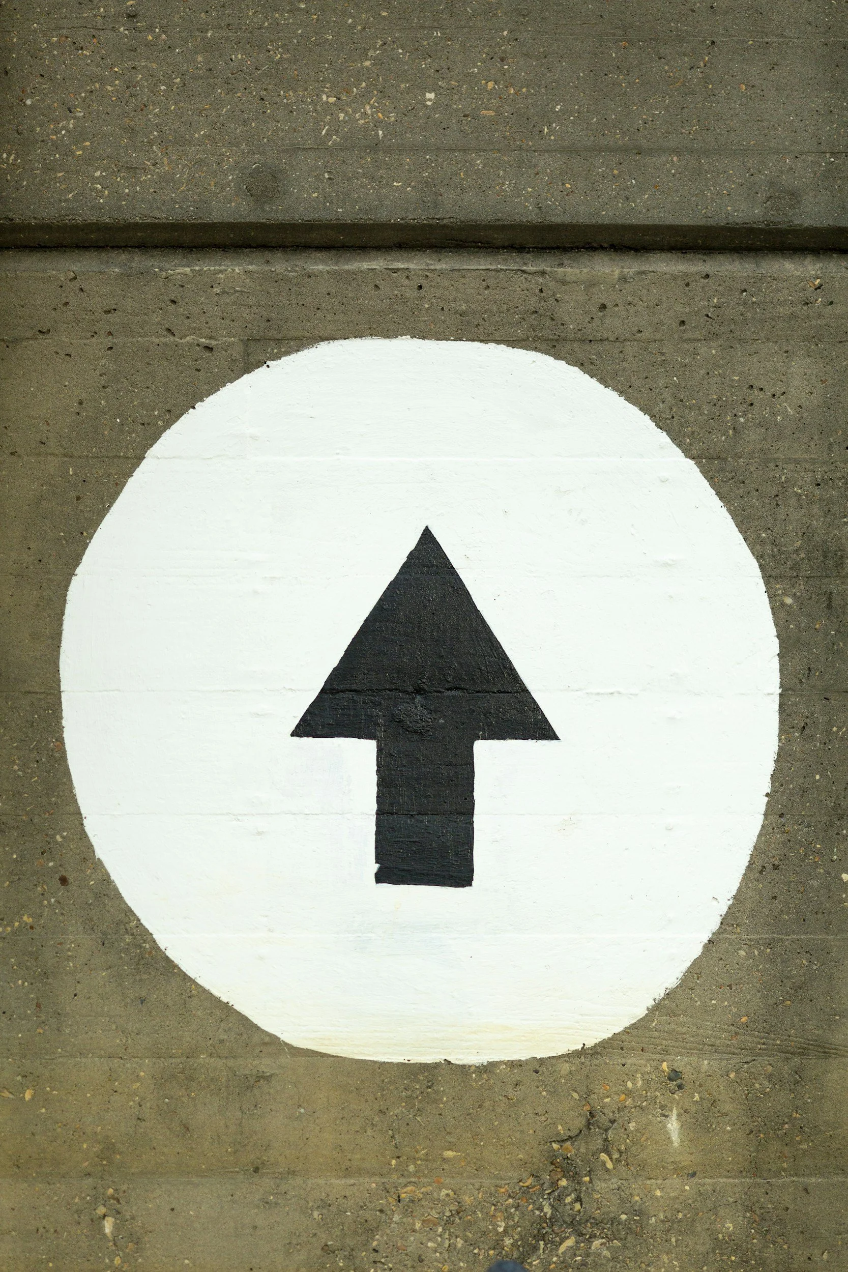 A circle painged on a brick wall with an arrow in the middle, pointing up.