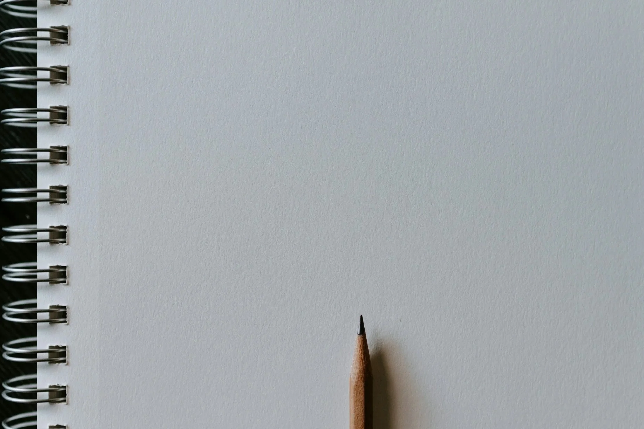 Close-up of a spiral-bound notebook with a blank white page and a sharpened pencil.
