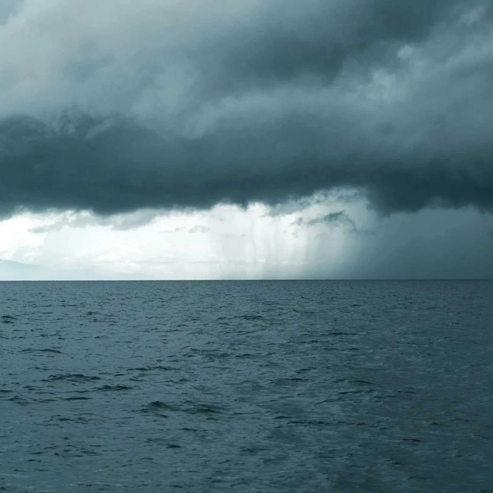 A stormy sea with dark clouds overhead and a ray of light on half of the horizon.