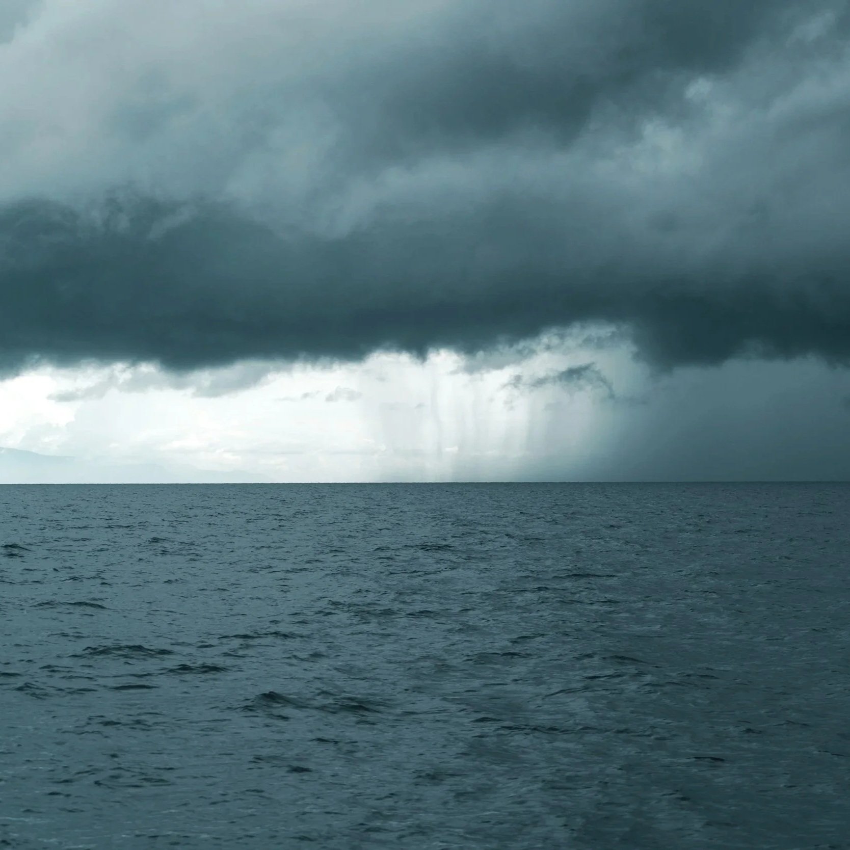 A stormy sea with dark clouds overhead and a ray of light on half of the horizon.