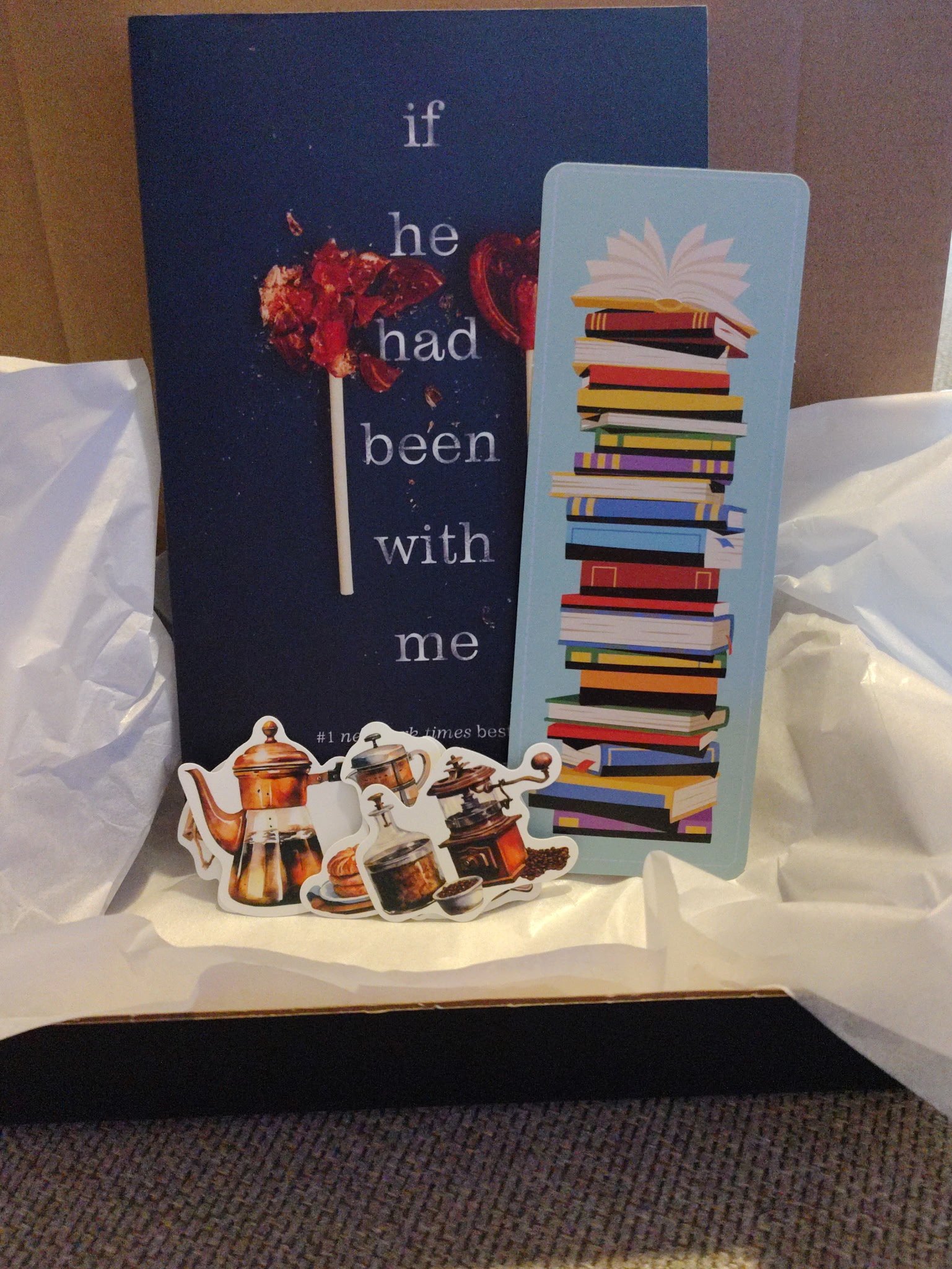 A gift box containing a sign with a heart and lollipop that says 'if he had been with me,' a blue bookmark with a pile of colorful books, and stickers of coffee pots and cups.